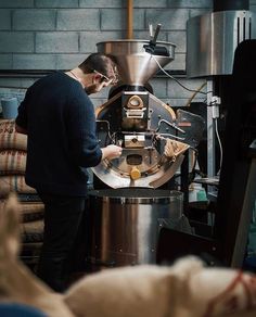 a man standing in front of a machine working on some kind of item that is being made into something