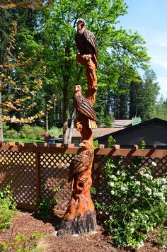 an eagle statue sitting on top of a tree stump in front of a wooden fence