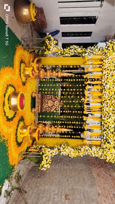 an arrangement of yellow flowers and bells in front of a green wall with gold decorations