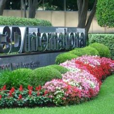 the entrance sign to the 3d international building in front of flowers and bushes on display