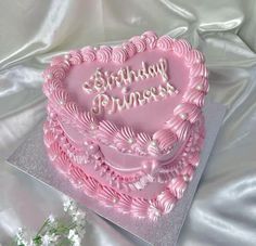 a pink heart shaped birthday cake sitting on top of a table