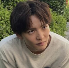 a young man sitting in front of some bushes