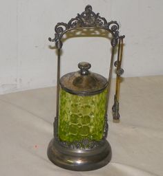 an old fashioned green glass tea kettle sitting on a white tablecloth with a metal stand