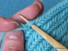 someone is knitting with a wooden needle on a blue knitted surface, and they are holding the yarn in their hands