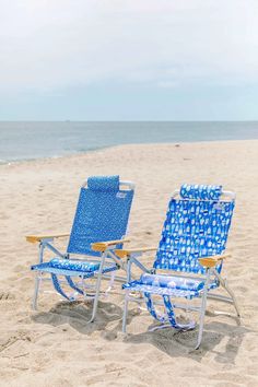 two blue lawn chairs sitting on top of a sandy beach next to the ocean,