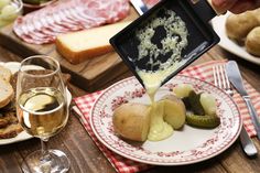 a person pouring cheese on top of potatoes and cucumbers with bread in the background