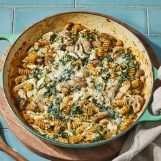 a skillet filled with pasta, meat and spinach on top of a wooden cutting board