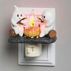 two white cats sitting on a shelf with a candle in the shape of a cat