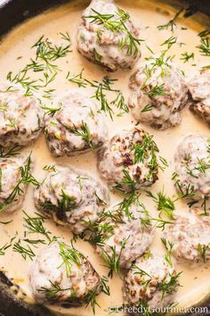 some meatballs are covered in gravy and garnished with fresh herbs