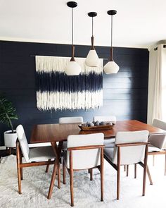 a dining room table with white chairs and black wall hangings above it, along with an area rug on the floor