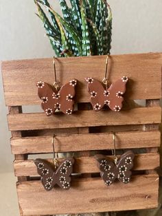 three brown and white butterfly shaped earrings hanging from hooks on a wooden rack next to a succulent plant