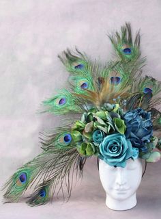 a white vase filled with blue flowers and peacock feathers on top of a headdress