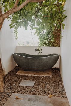 a bathtub sitting under a tree in the middle of a room with rocks on the floor