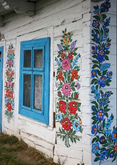 an old building with painted flowers on the side and blue window panes in front