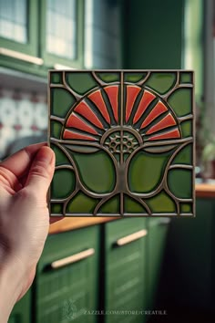 a person holding up a piece of art glass in their hand with green cabinets behind it