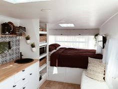 a small bedroom with a bed, sink and window in the back wall is decorated with black and white tiles