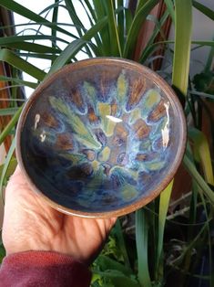 a hand holding a small bowl in front of some potted plants and greenery