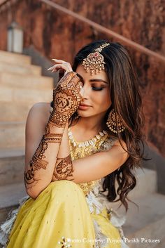 a woman in a yellow dress holding her hands to her face with henna on