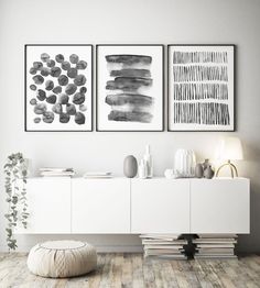 two black and white paintings on the wall next to a table with vases, books and other items