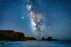 the milky shines brightly in the night sky above an ocean and rocky shore line