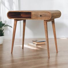 a wooden desk with two drawers sitting on the floor next to a potted plant