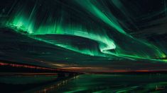 the aurora bore is glowing green in the night sky over water with stars and clouds