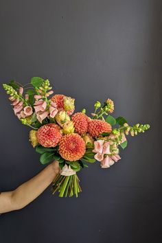 a bouquet of flowers is being held by a person's hand against a gray wall