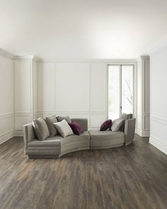 a living room with white walls and wood flooring that has a curved couch in the middle