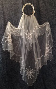 a white veil with flowers on it hanging from a wall next to a black background