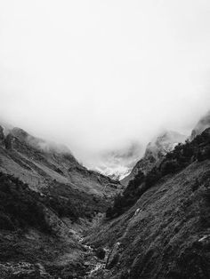 a black and white photo of mountains in the distance with clouds coming down on them