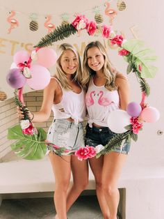 two women standing next to each other in front of a wall with balloons and flamingos