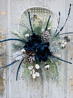 a wreath with pine cones and blue ribbon hanging on a white wooden door decorated with ornaments