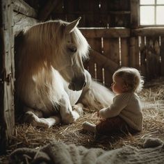 a baby sitting next to a horse in a barn