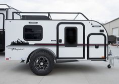 a white trailer with black trim parked in a parking lot next to other trailers and buildings