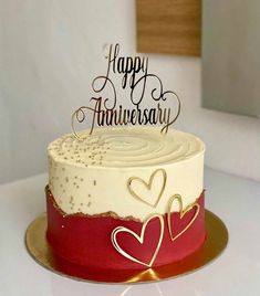 a white and red cake sitting on top of a table next to a knife with the words happy anniversary written on it