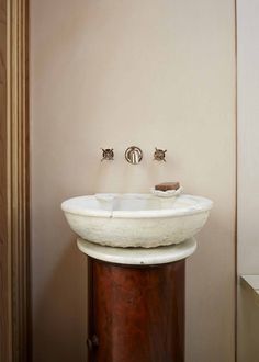 a white sink sitting on top of a wooden pedestal next to a wall mounted faucet