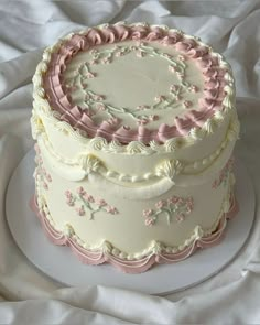 a three layer cake with pink and white frosting on a plate, sitting on a bed sheet