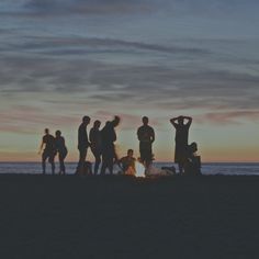 a group of people standing around a fire on the beach