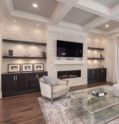 a living room with white couches and a glass coffee table in front of a fireplace