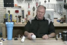 a man sitting at a table with an object in front of him and several other tools on the wall behind him