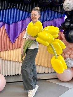 a woman standing in front of balloons with yellow flowers on them and smiling at the camera