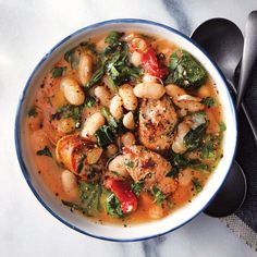 a white bowl filled with food on top of a marble counter next to black spoons