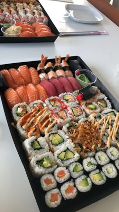 two trays filled with different types of sushi on top of a white table