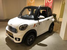 a small white car is parked in a showroom with signs on the wall behind it