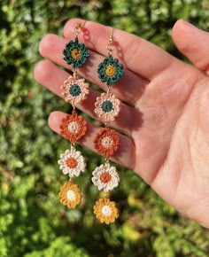 a hand holding four crochet flower earrings in it's left hand,