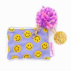 TAYLOR ELLIOTT DESIGNS Details ♥ Size: 4.75" x 3.5" ♥ Embroidered smiley pattern on front ♥ Purple gingham pattern on backside ♥ Durable cotton canvas material ♥ Black polka dot interior lining ♥ Gold zipper accents and gold keychain clasp on zipper ♥ Colorful yarn pom pom, acrylic and acrylic smiley keychain details ♥ Imported SKU: POUCH-23 Smiley Keychain, Smiley Pattern, Keychain Pouch, Purple Gingham, Gold Keychain, Bath Gift Set, Yarn Pom Pom, Bath Gift, Gingham Pattern