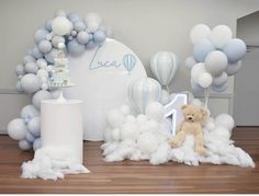 a baby's first birthday party with balloons, cake and teddy bear on the floor