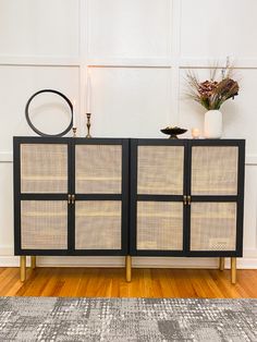 a black and gold sideboard sitting on top of a wooden floor next to a vase with flowers