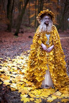 a woman dressed in yellow leaves stands on the ground with her arms around her body