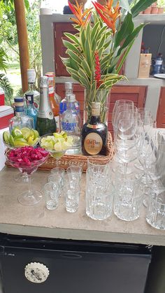 an assortment of wine glasses and liquor bottles on a table with flowers in vases